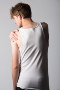 外国人の男性がタンクトップで肩を抑えている後ろ姿